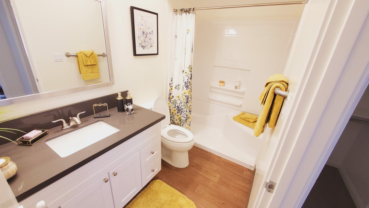 A neatly organized bathroom with yellow accents featuring a shower, sink, and toilet.