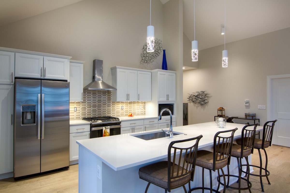 A modern kitchen featuring stainless steel appliances, a spacious countertop with bar stools, and stylish pendant lighting.