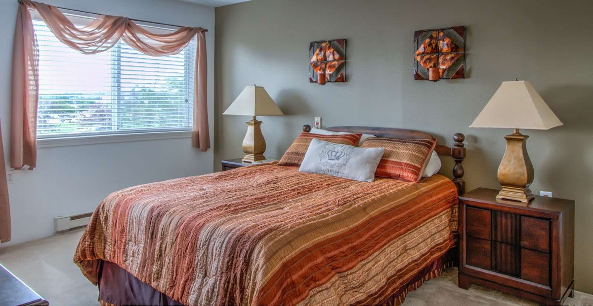 A cozy bedroom with warm-toned bedding and a lamp by the window.