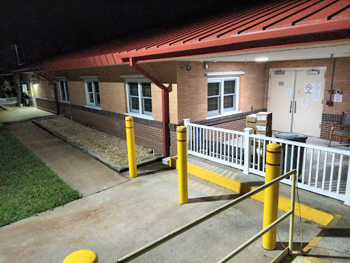 Exterior view of a commercial building at night, featuring yellow safety poles and a paved walkway.