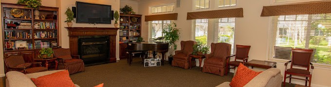 A cozy living room with a piano, armchair, and bookshelf by the windows.