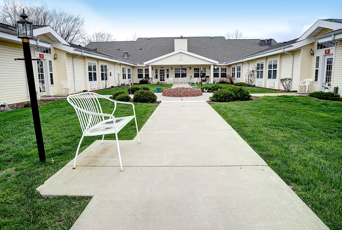 A pathway leading to a building, flanked by grass and a bench.