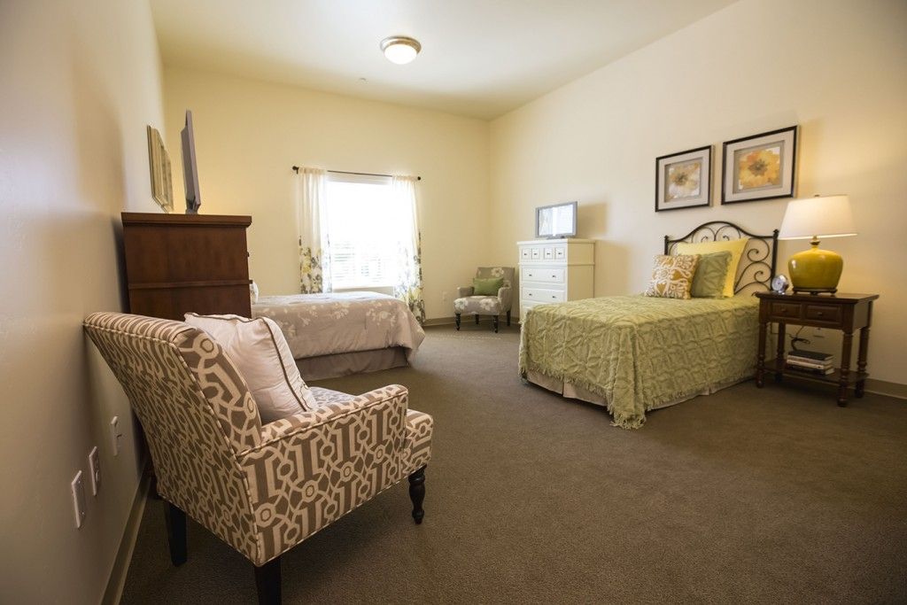 A cozy bedroom with two beds, a patterned chair, and soft lighting.