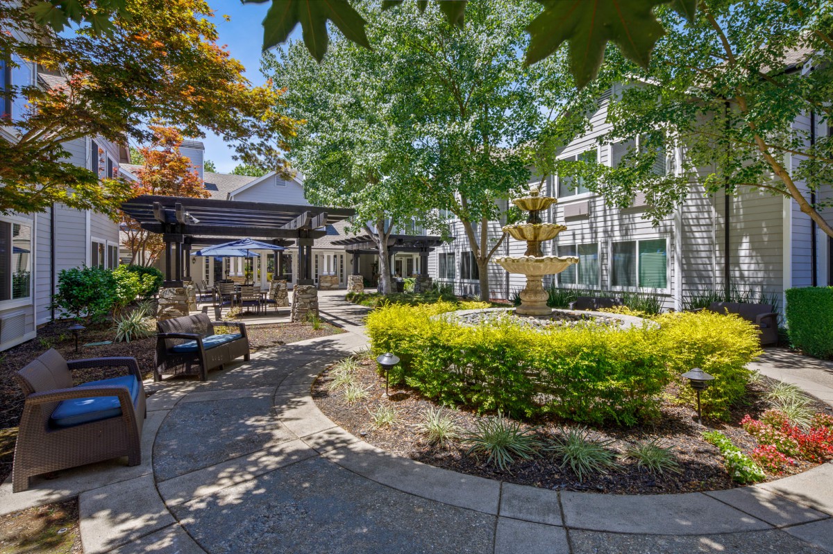 A beautifully landscaped courtyard with a fountain, surrounded by trees and seating areas.