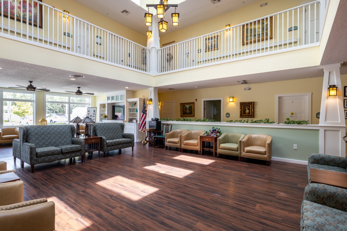 A spacious lobby with comfortable seating and a wooden floor, featuring a balcony and overhead lighting.