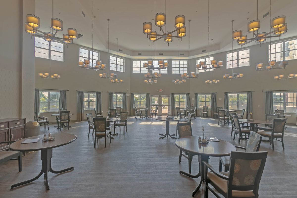 A spacious dining room with large windows, multiple tables and chairs, and elegant chandeliers.