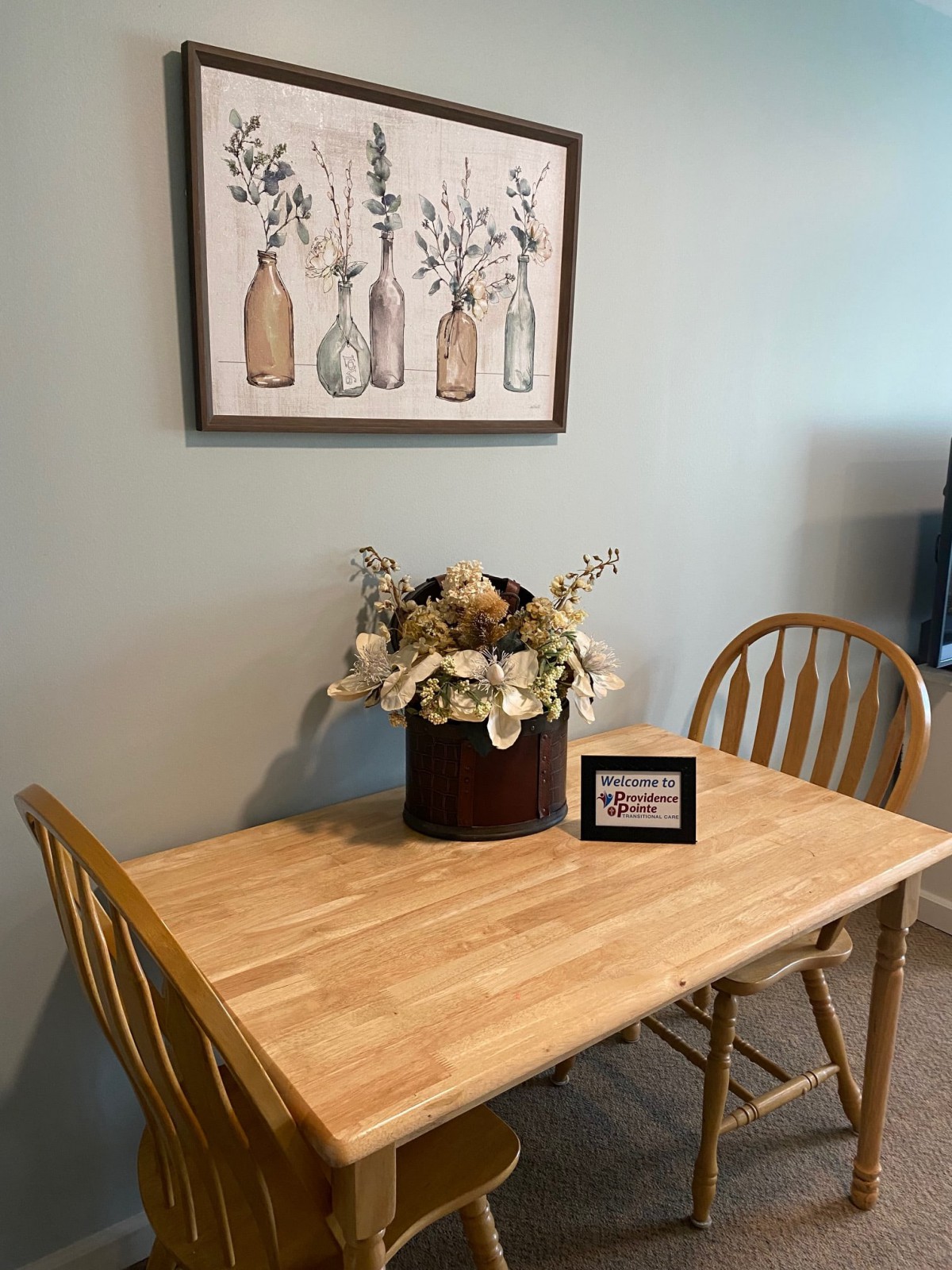 A cozy dining setup with a wooden table and chairs, adorned with floral decorations and wall art.