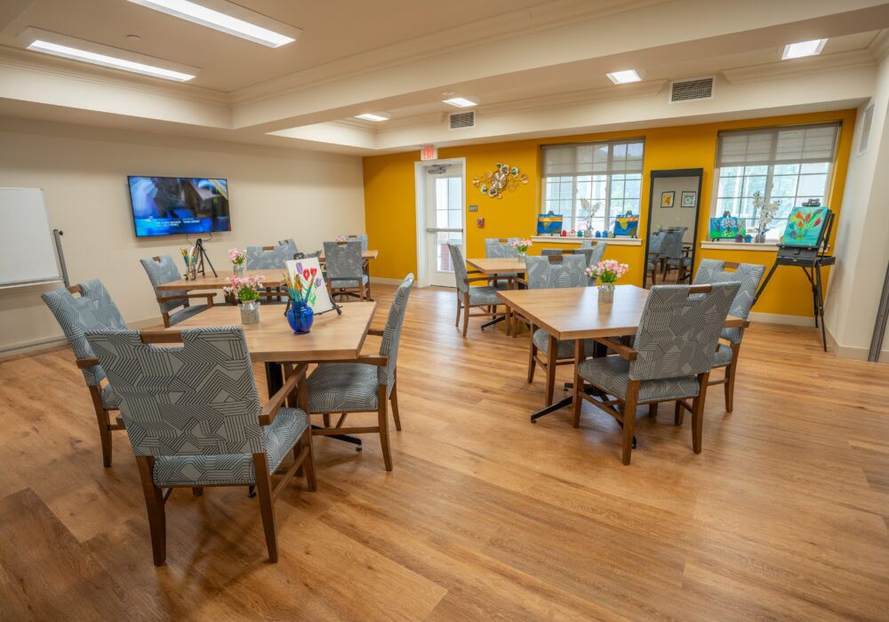 A cozy dining area with several tables and chairs, a television on the wall, and bright yellow accent walls.