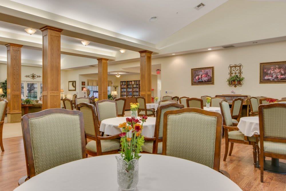 An elegant dining room with tables set for a meal, featuring floral centerpieces and cozy lighting.