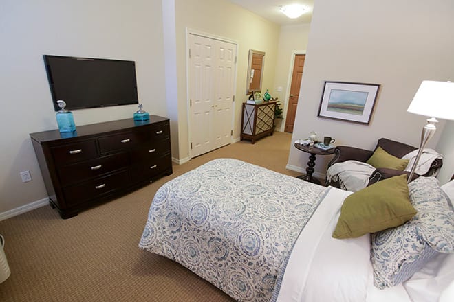 A cozy bedroom with a patterned bedspread, television, and dresser.