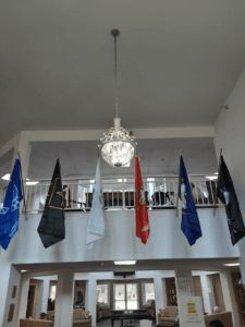 A display of various military flags in an atrium with a chandelier.