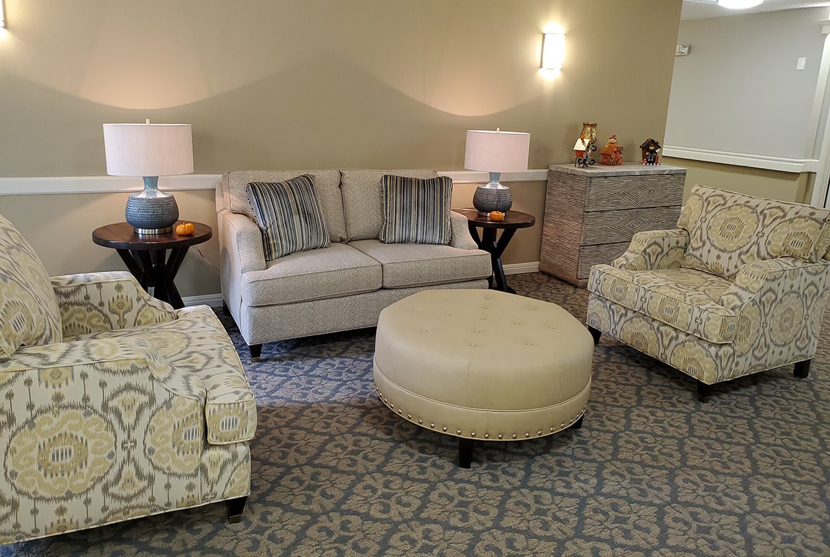 A cozy living room with a sofa, chairs, and a central ottoman, accented by warm lighting from two lamps.
