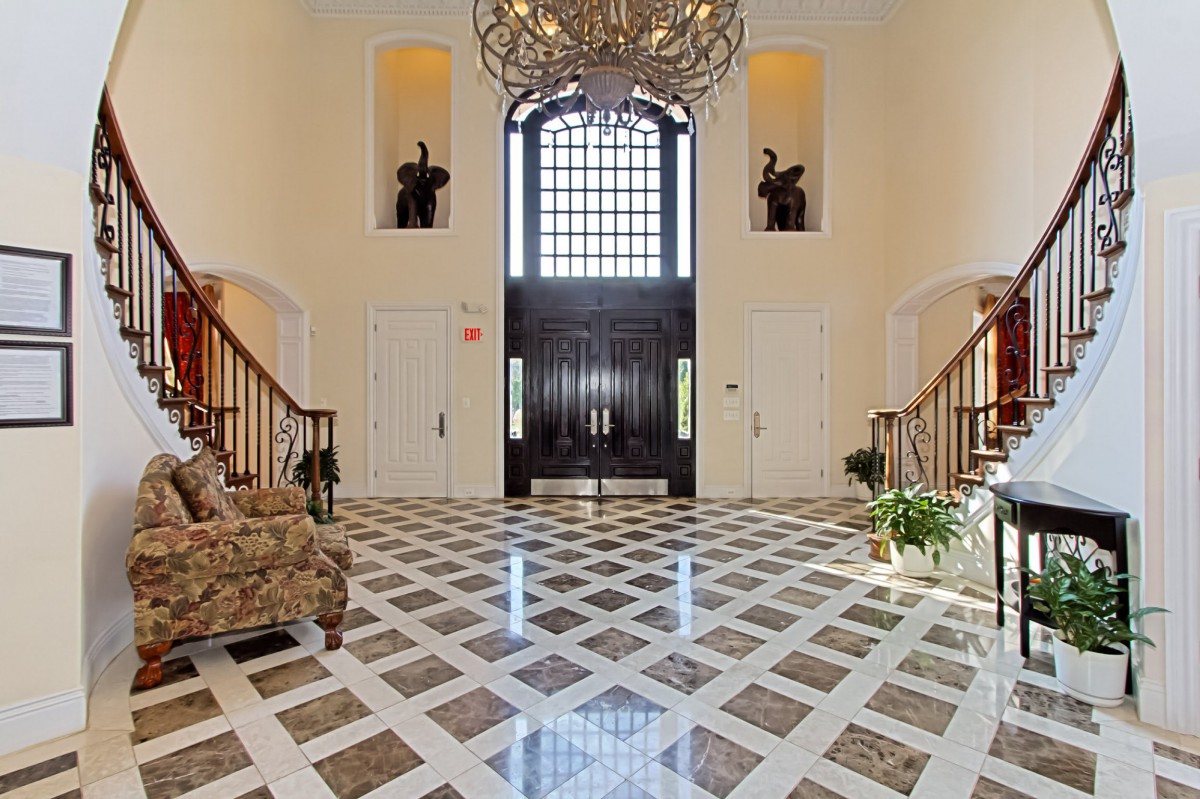 A luxurious foyer with a grand chandelier, marble flooring, and two elegant staircases.