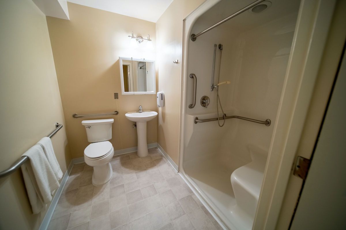An accessible bathroom with a shower, toilet, sink, and grab bars.
