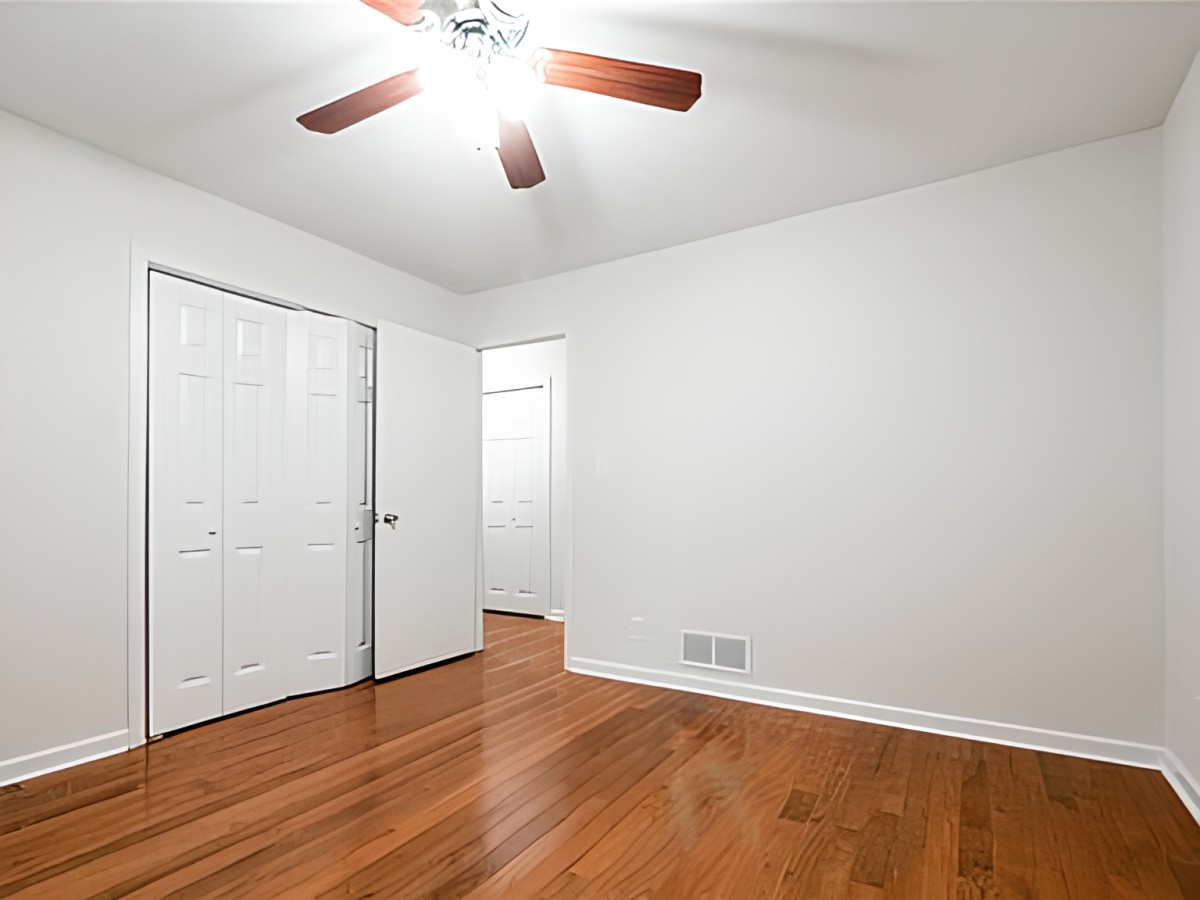 An empty room featuring wooden floors and a ceiling fan.