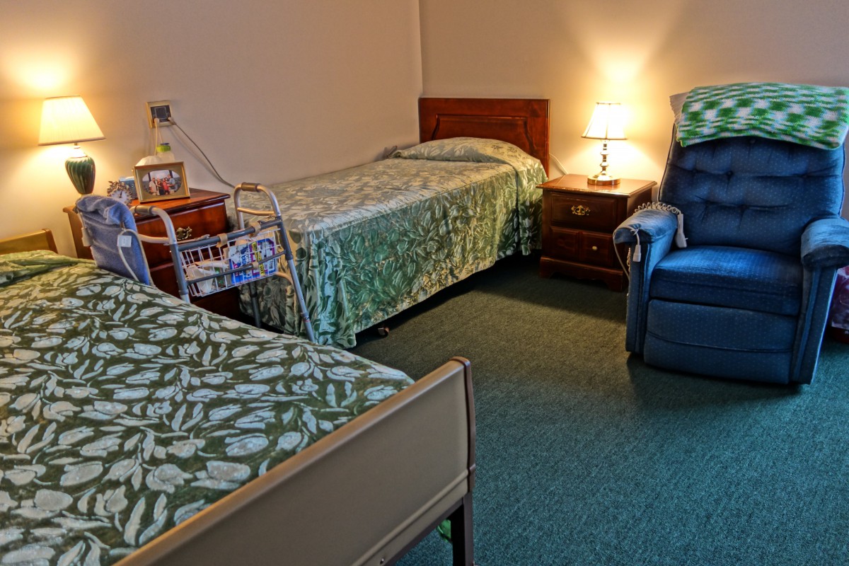A cozy hospital room with two beds, a nightstand, and a comfortable chair.
