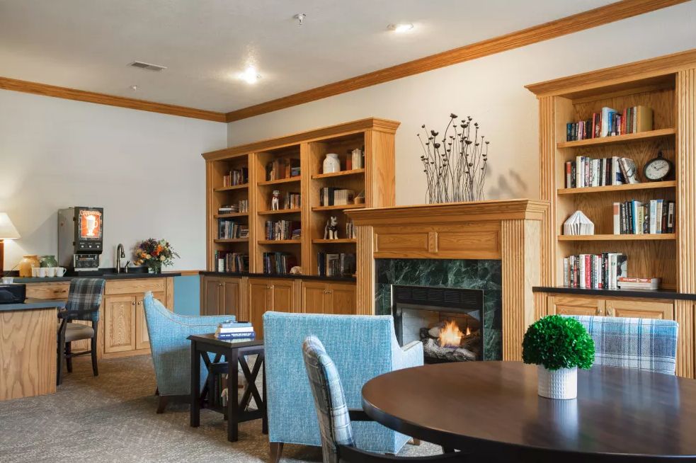 A cozy library with comfortable seating, bookshelves, and a warm fireplace.