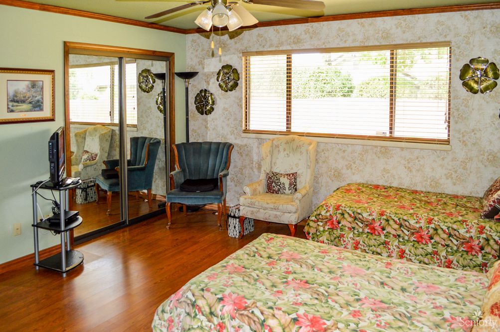 A cozy bedroom with floral bedding, mirrored closet doors, and comfortable armchairs.