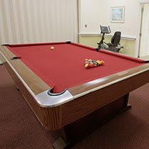 A room featuring a pool table with red felt next to exercise equipment.