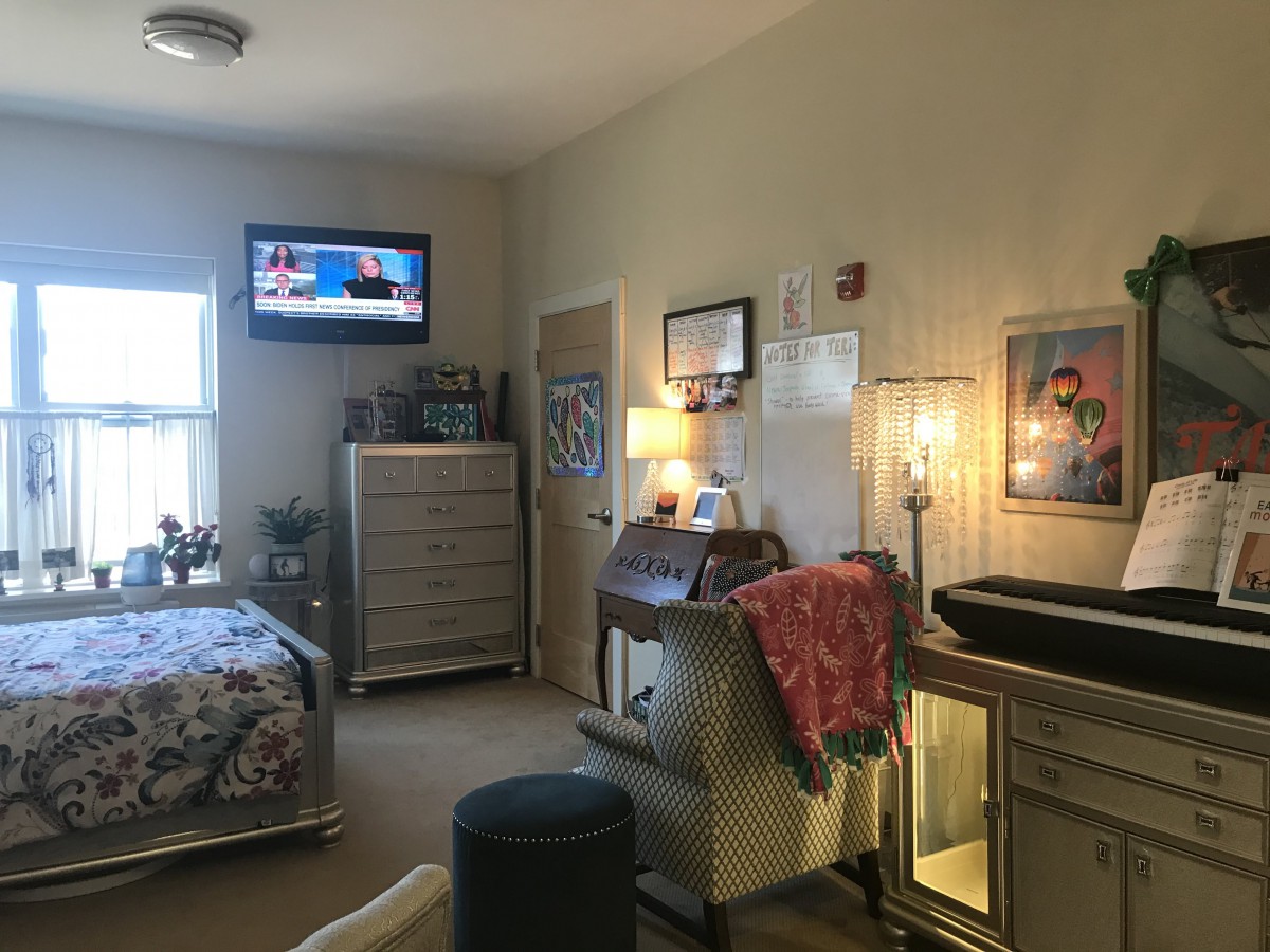 A cozy bedroom with furniture, a TV mounted on the wall, and soft lighting.
