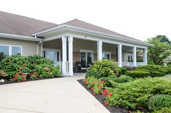 A single-story building with a front porch, featuring white columns, surrounded by landscaped gardens and shrubs.