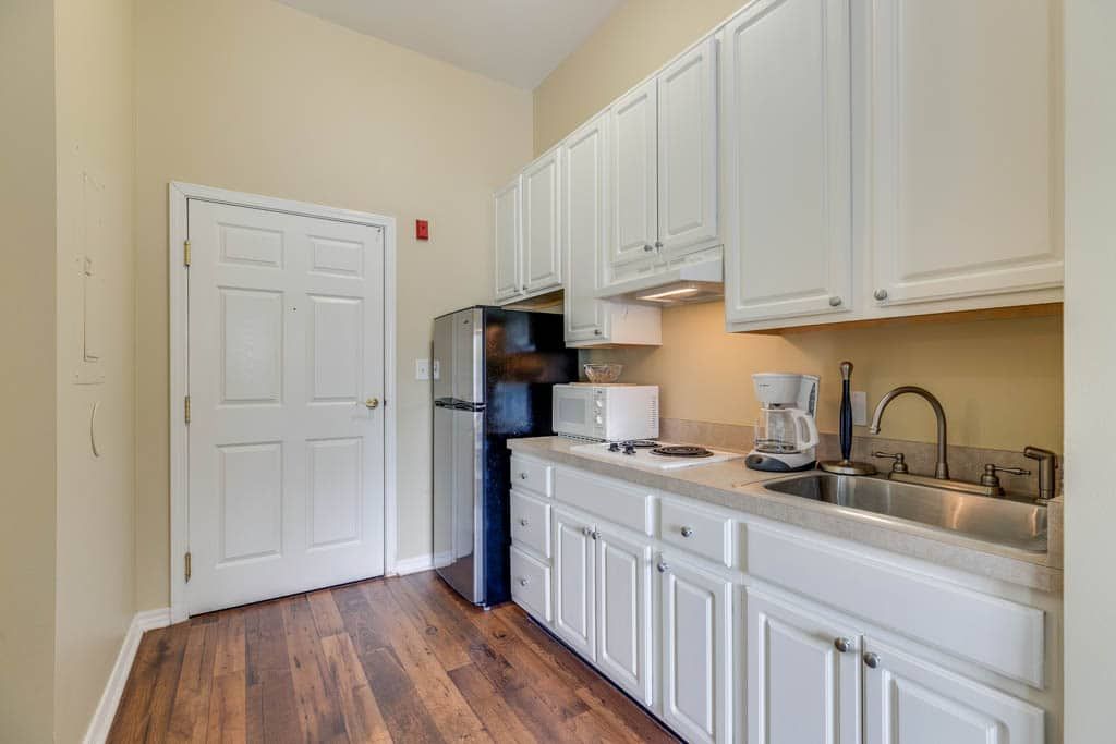 A modern kitchen with white cabinets, stainless steel appliances, and wooden flooring.