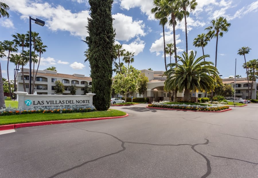 Entrance of a residential apartment complex surrounded by palm trees and well-maintained landscaping.