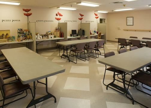An empty classroom with desks, chairs, and computers, featuring tiled flooring and overhead lighting.