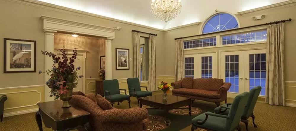 A well-furnished living room with a chandelier, comfortable seating, and large windows.