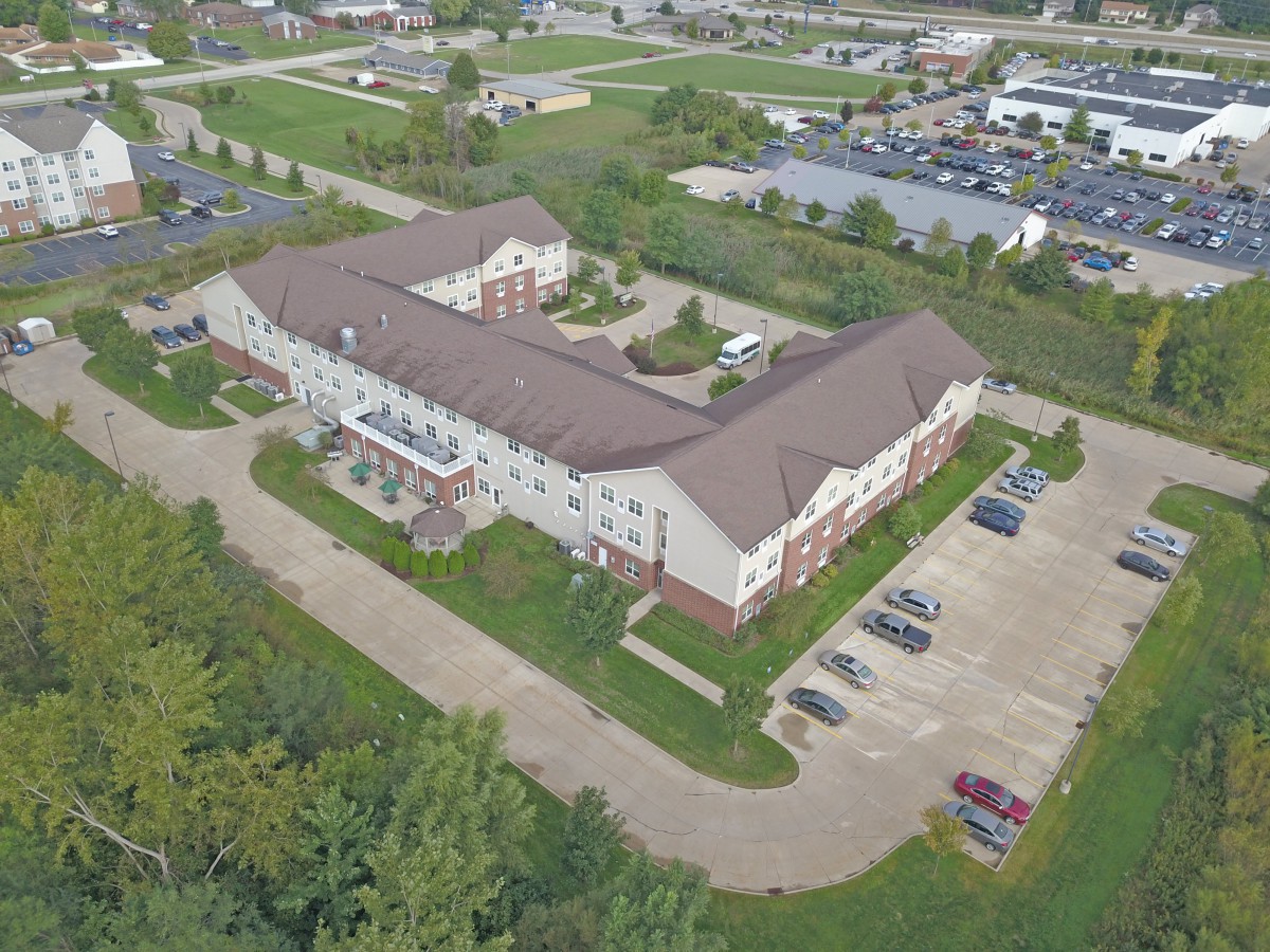 Aerial view of a large building with a parking lot surrounded by greenery and roads.
