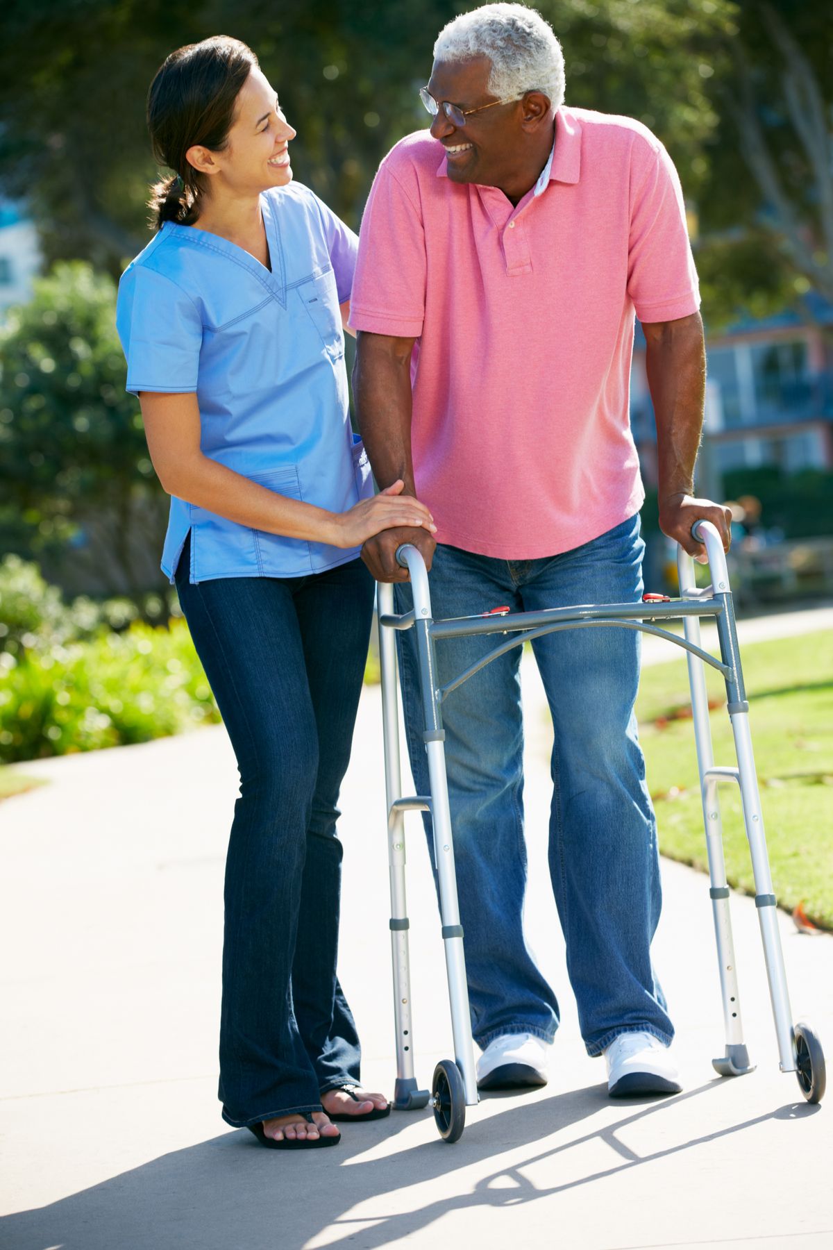 A caregiver assists an elderly person using a walker outdoors.