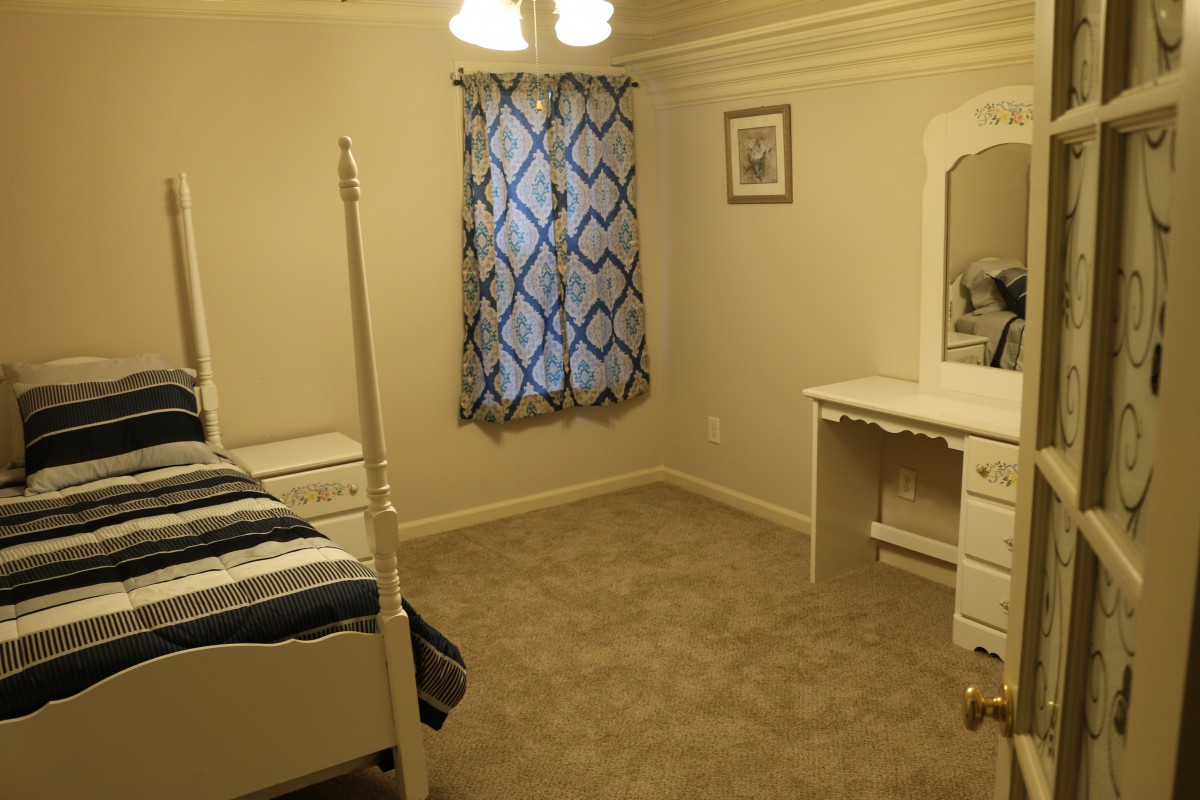 A simple bedroom with a bed, vanity dresser, and carpeted floor.