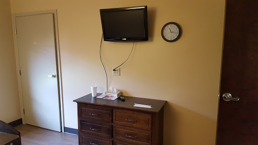 A simple room featuring a wall-mounted television and a clock above a wooden dresser.