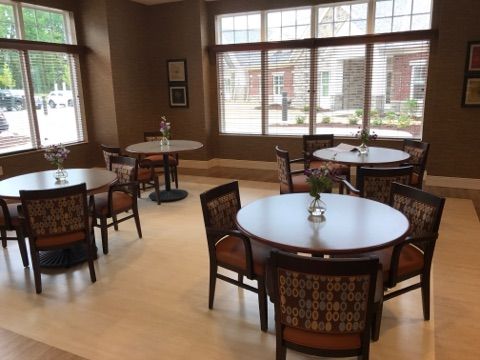 A cozy dining area with round tables and chairs, well-lit by large windows.
