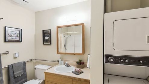 A bathroom with a sink, mirror, toilet, and a stacked washer and dryer unit.
