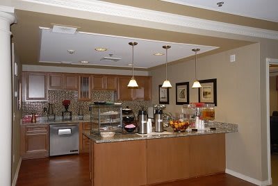 A modern kitchen interior featuring wooden cabinetry, a central island with pendant lighting, and various appliances and decor.