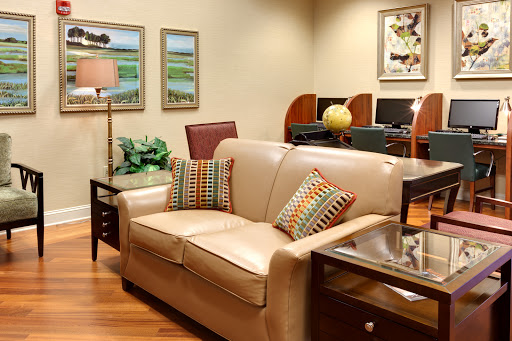 A cozy living room setup featuring a beige sofa with decorative pillows, surrounded by tasteful artwork and greenery.