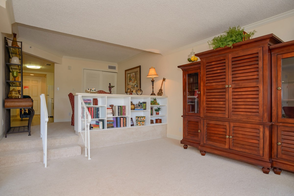 A cozy living room area featuring a bookshelf with various books and decorations, alongside wooden furniture and a warm lamp.