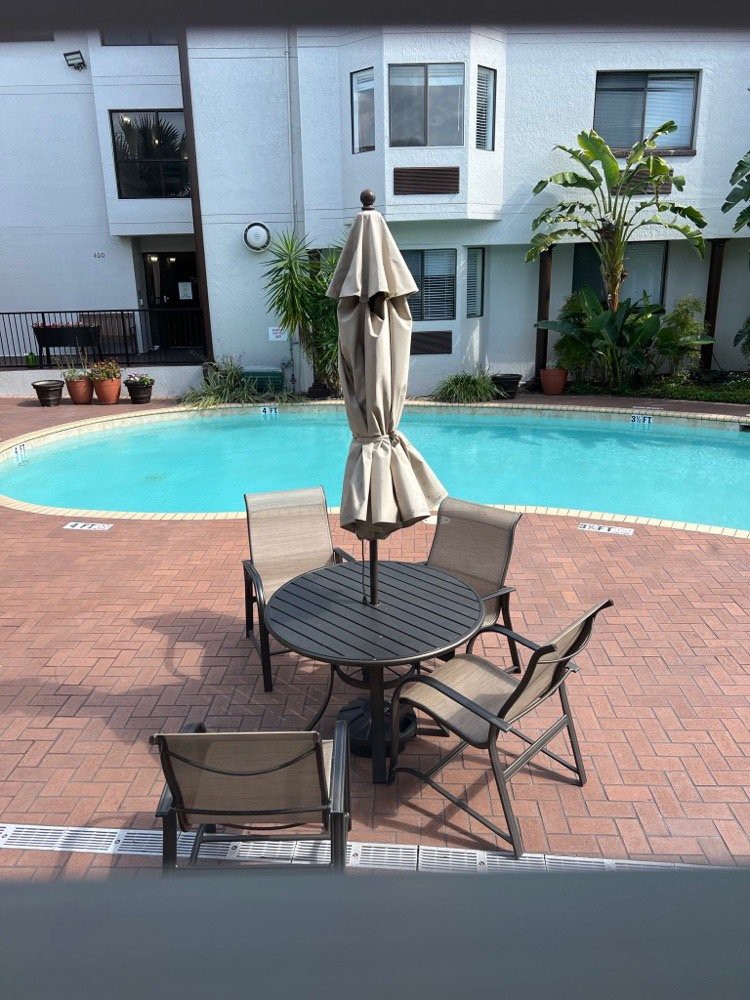 A serene outdoor pool area featuring a round table with chairs and an umbrella.