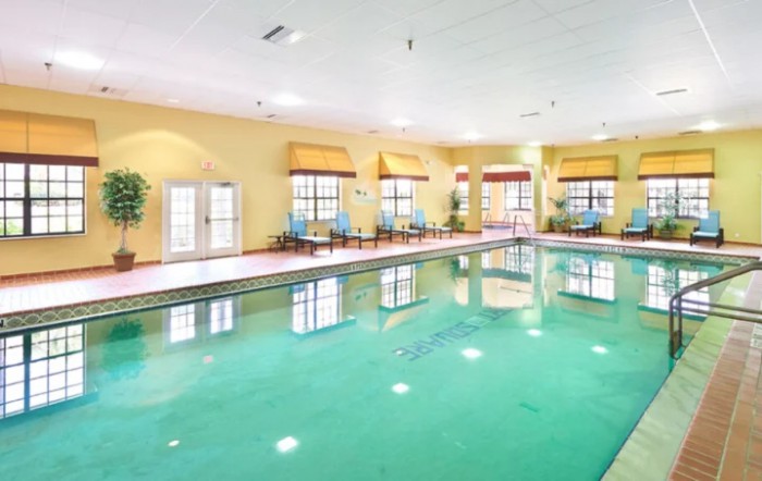 An indoor swimming pool with ample natural light and seating arrangements along the side.