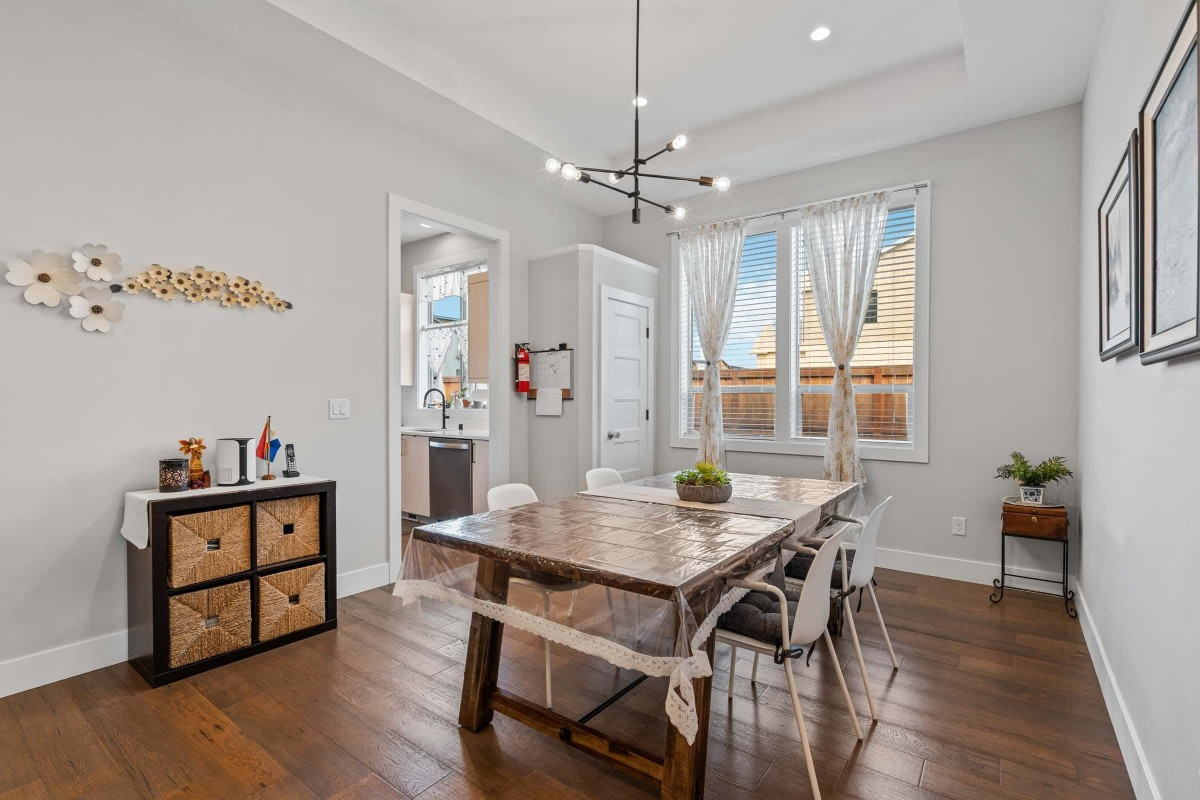 A modern dining room with a wooden table and stylish chandelier, featuring large windows with curtains.