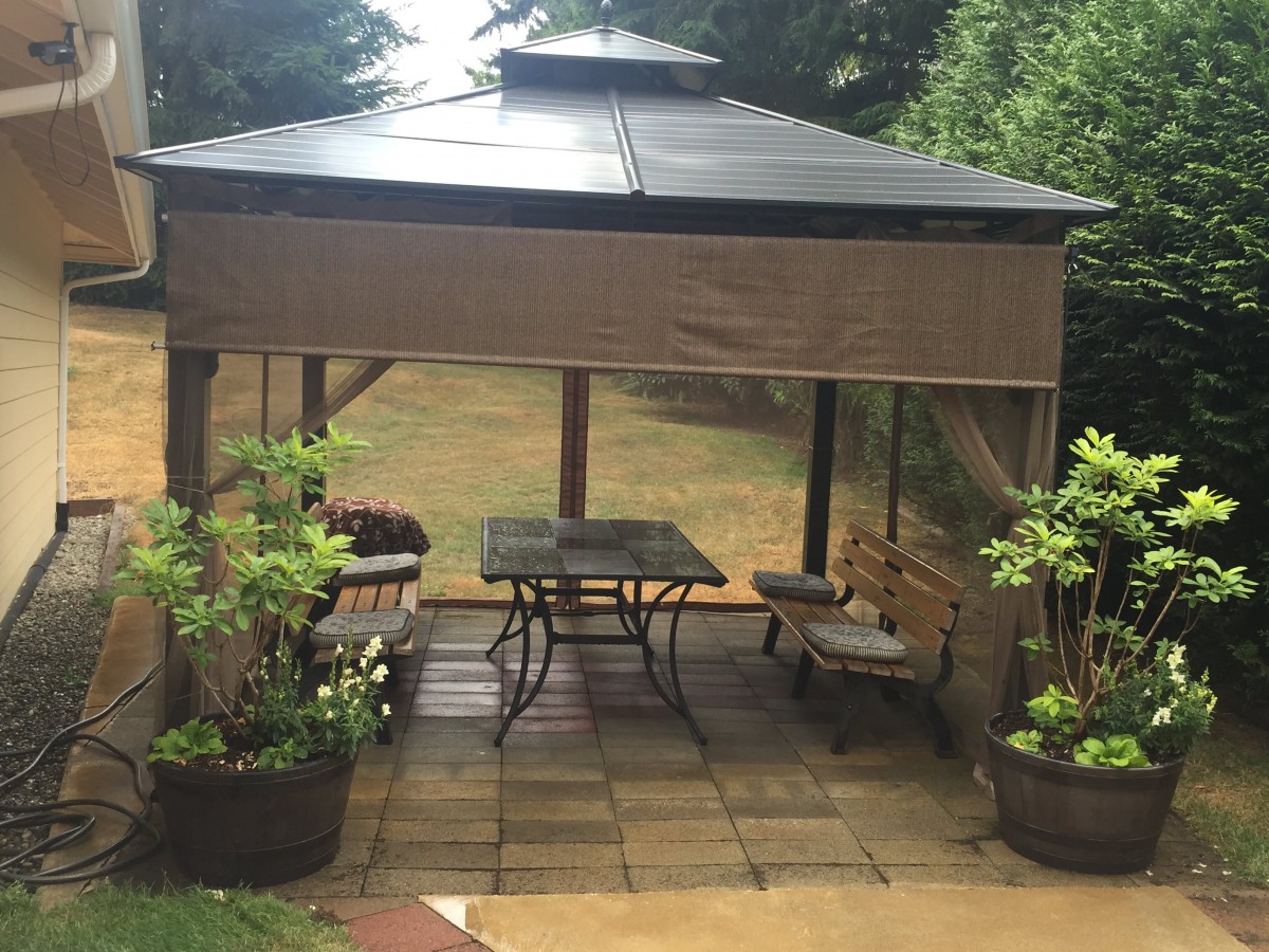 A cozy outdoor patio area with a gazebo and seating surrounded by plants.