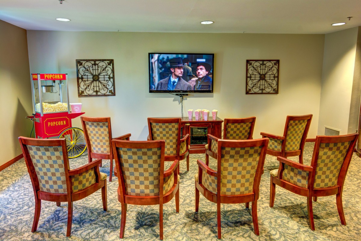 A small theater room with chairs facing a television screen playing a movie, featuring a popcorn machine in the corner.