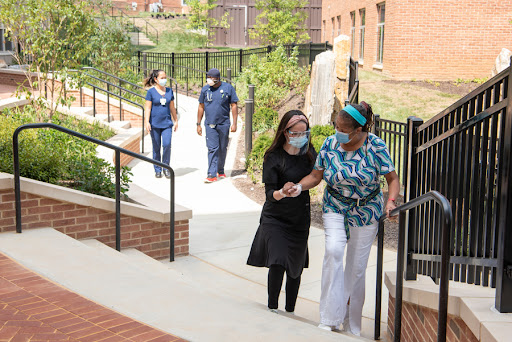 Healthcare workers assist a person as they walk together outdoors in a supportive environment.