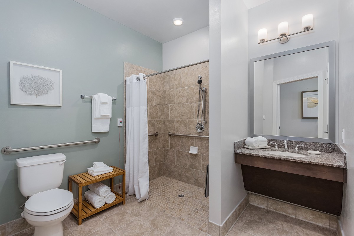 An accessible bathroom with a walk-in shower, toilet, sink, and neatly folded towels.