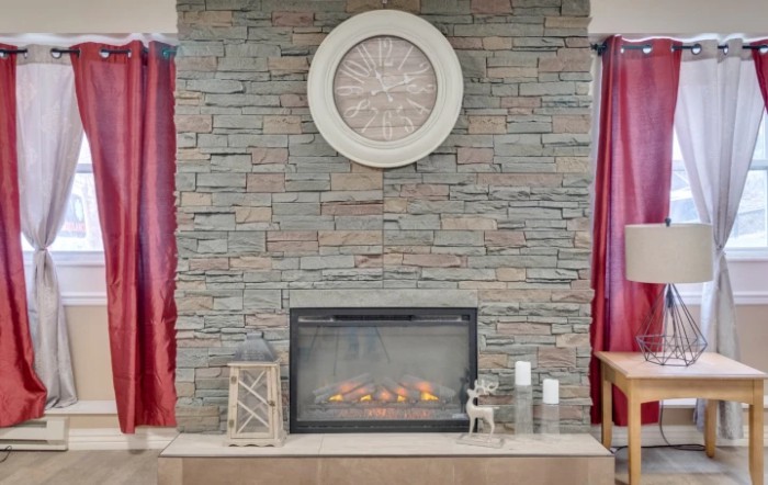 A cozy living room with a stone fireplace, decorated with candles, a lantern, and a large clock above the mantel.