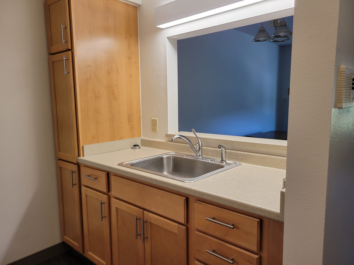 A kitchen area featuring wooden cabinets, a stainless steel sink, and a bright countertop.