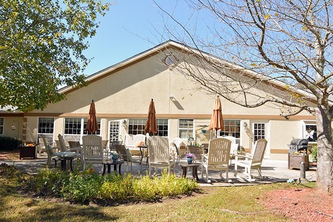A sunny patio area with tables, chairs, and umbrellas in front of a building.