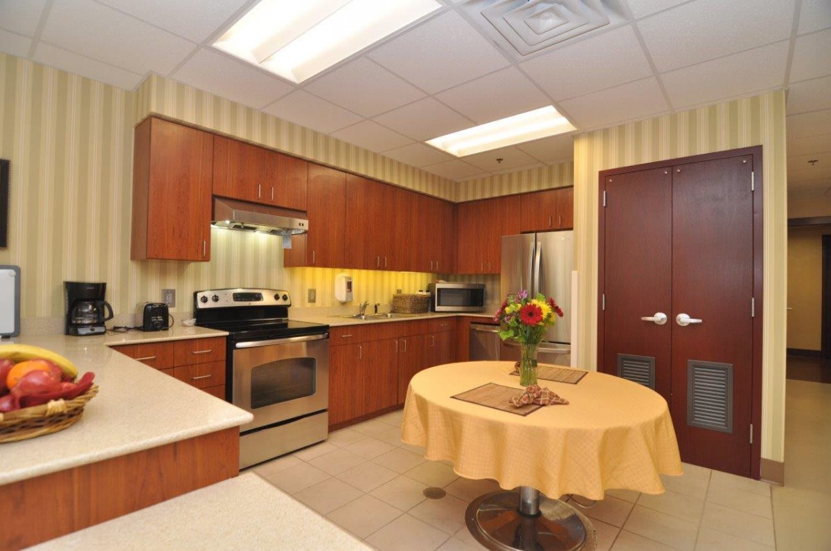 A modern kitchen with stainless steel appliances and wood cabinets, featuring a table with a flower vase.