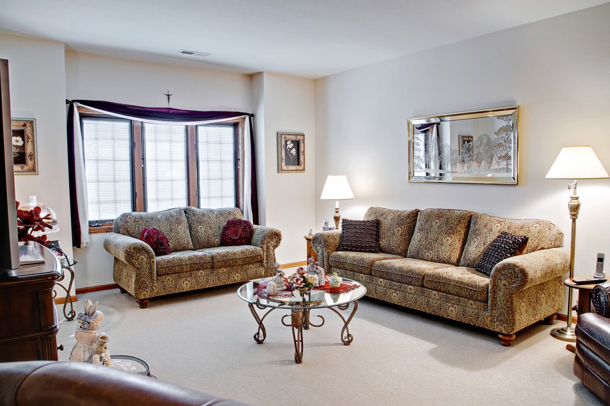 A cozy living room featuring two sofas, a glass coffee table, a lamp, and a large mirror.